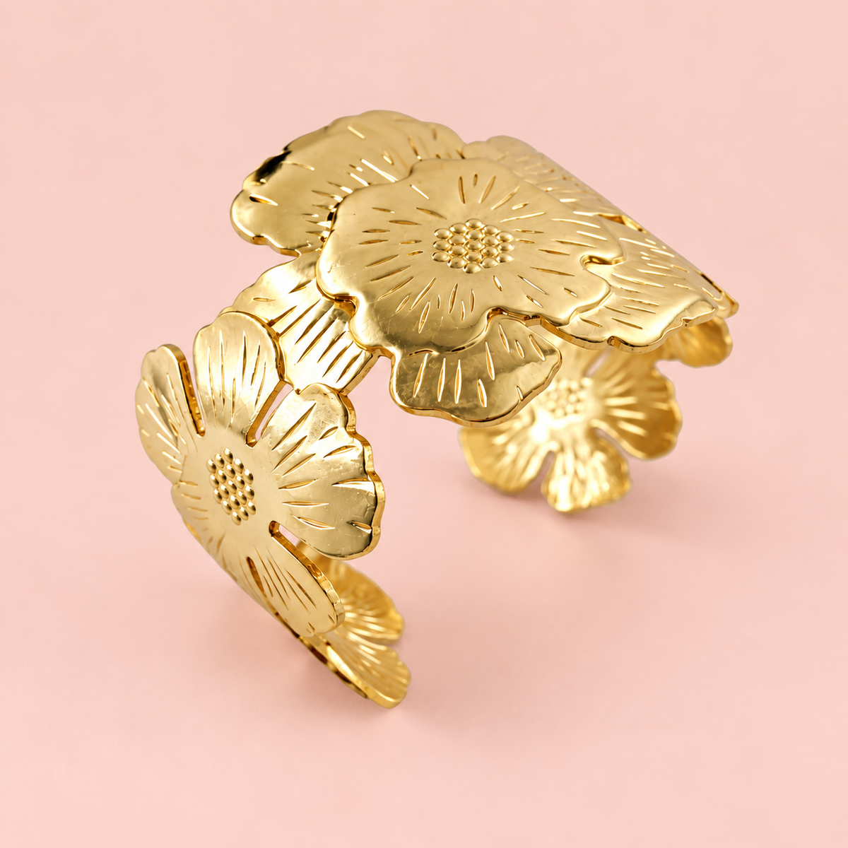 Wide gold-tone garden bloom floral cuff bracelet for women featuring large overlapping engraved flower motifs with sunburst petal lines and dotted centres, open-back kada style on pink background, by EVYRAA