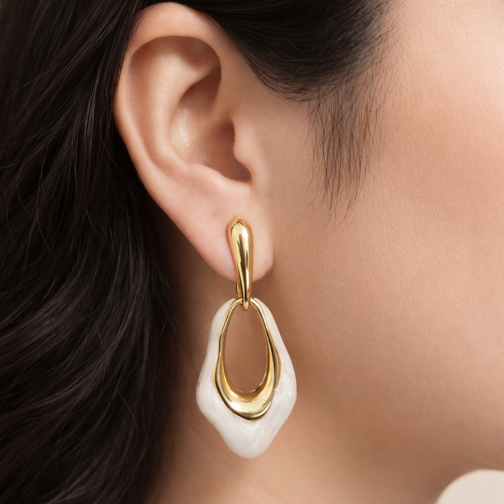 Gold and white earrings worn by a person with dark hair.