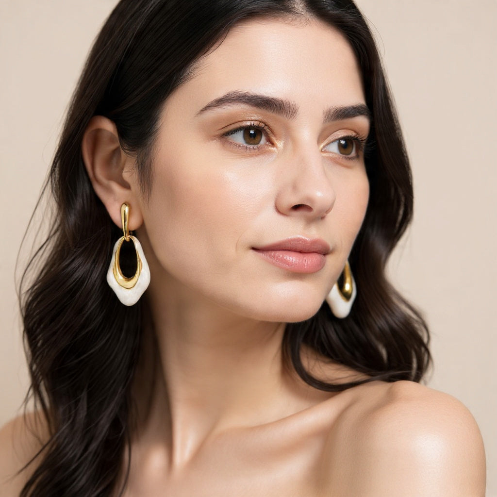 Woman wearing gold and black earrings against a beige background
