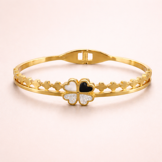 Gold bracelet with a clover-shaped charm on a light pink background
