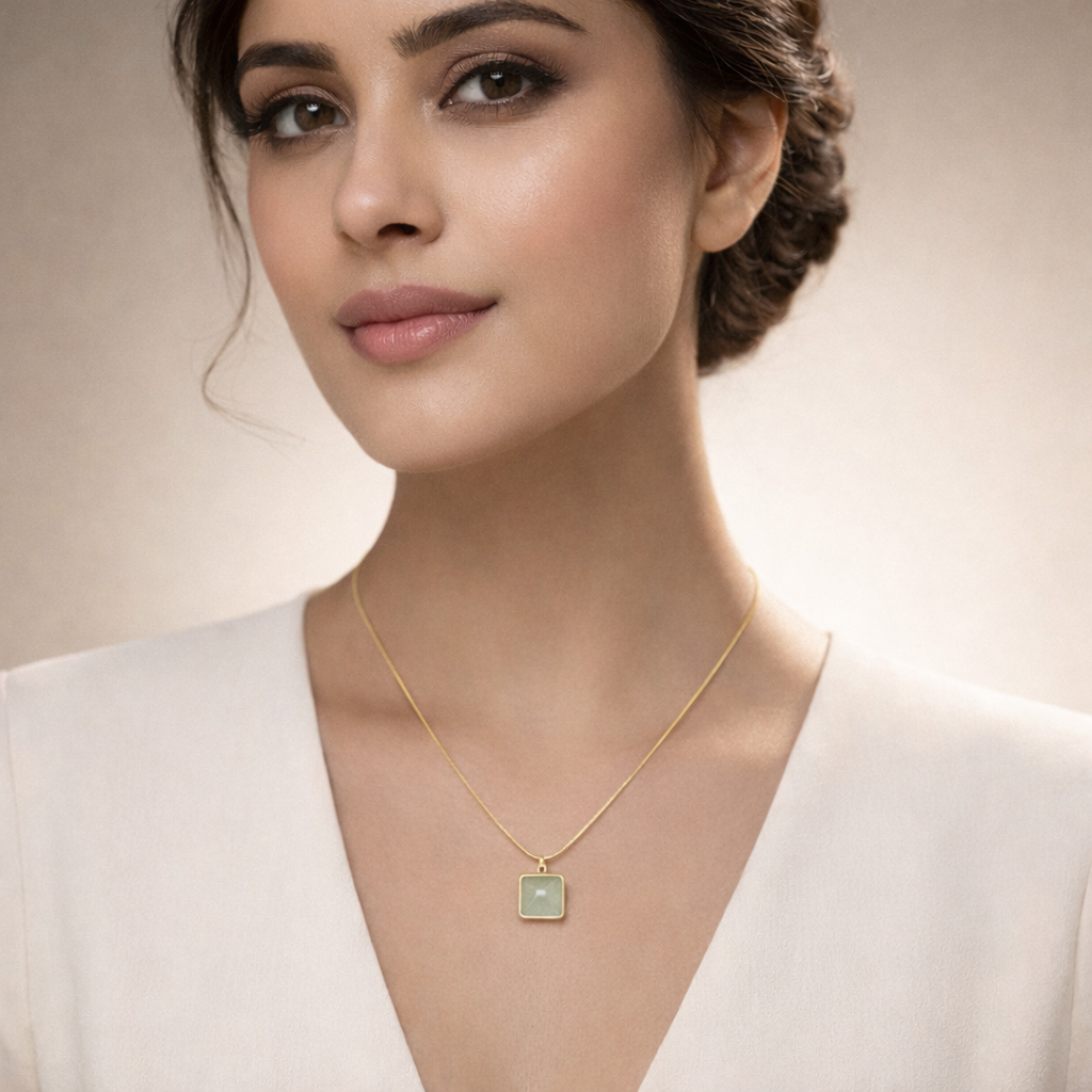 Woman wearing a gold necklace with a green pendant against a neutral background