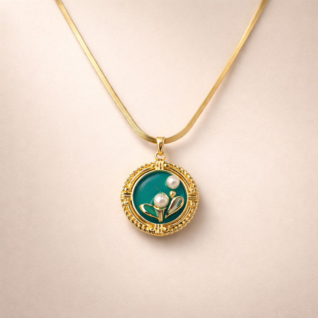 Gold necklace with a green pendant featuring a pearl and leaf design on a beige background