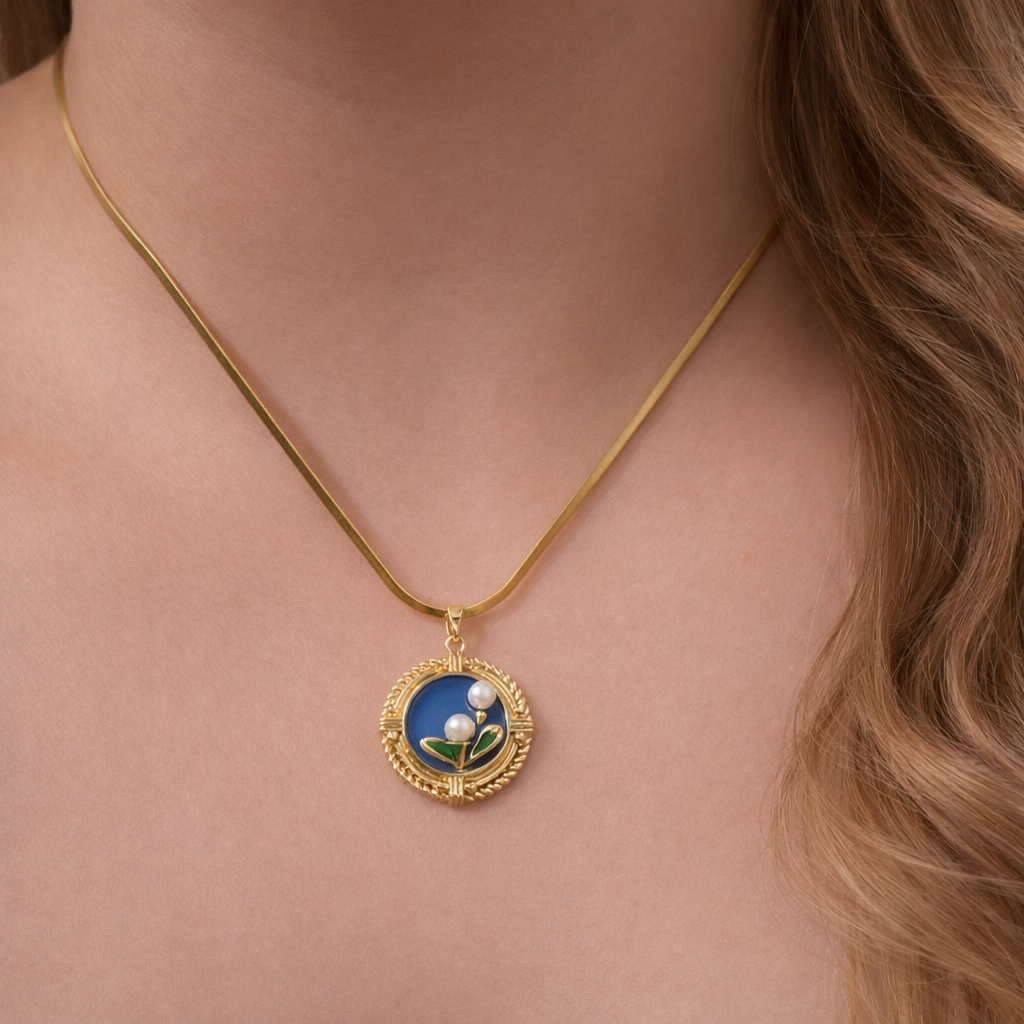 Gold necklace with a blue pendant featuring a floral design on a person's neck.