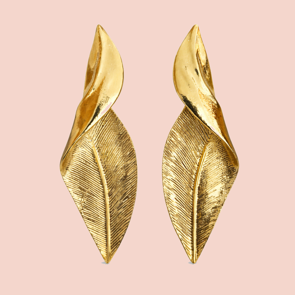 Gold leaf-shaped earrings on a pink background