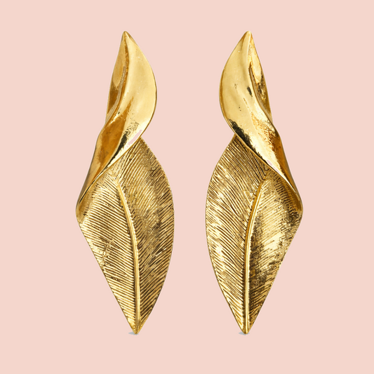 Gold leaf-shaped earrings on a pink background